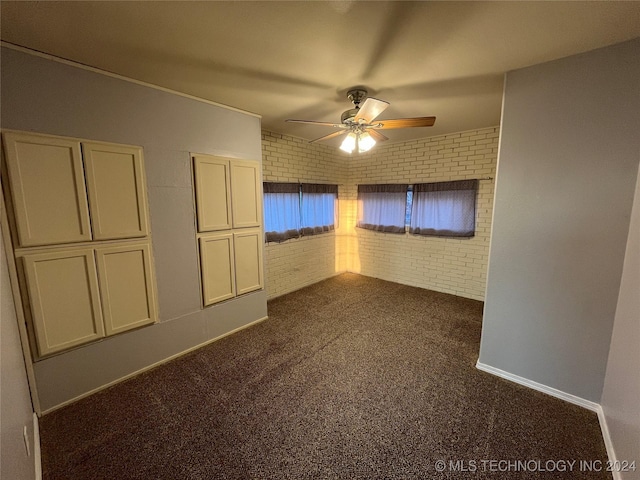 carpeted empty room featuring ceiling fan and brick wall