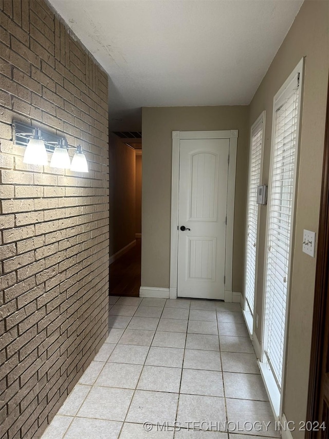 hallway with light tile patterned flooring and brick wall