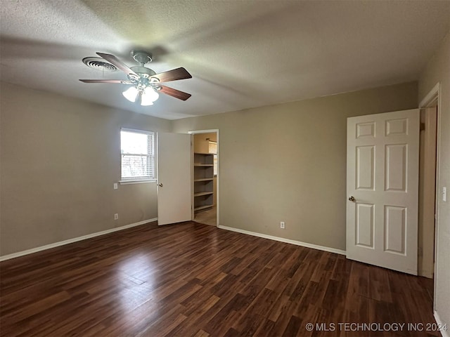 unfurnished bedroom with a spacious closet, ceiling fan, dark wood-type flooring, a textured ceiling, and a closet