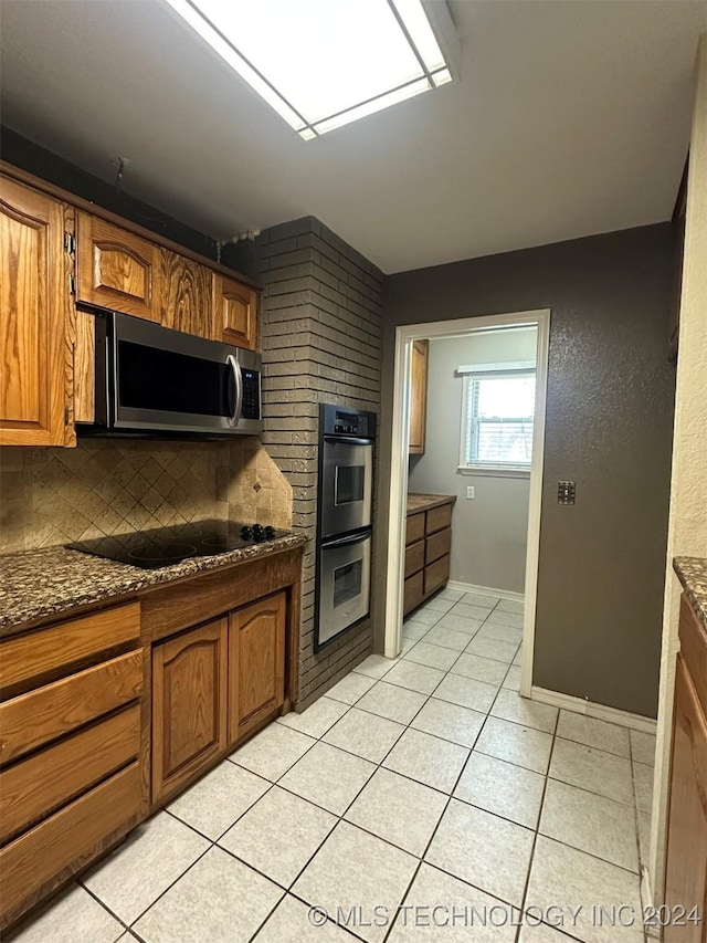 kitchen with stainless steel appliances, tasteful backsplash, dark stone counters, and light tile patterned flooring