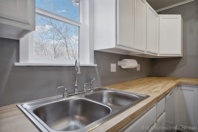 kitchen featuring white dishwasher, crown molding, sink, white cabinetry, and butcher block counters