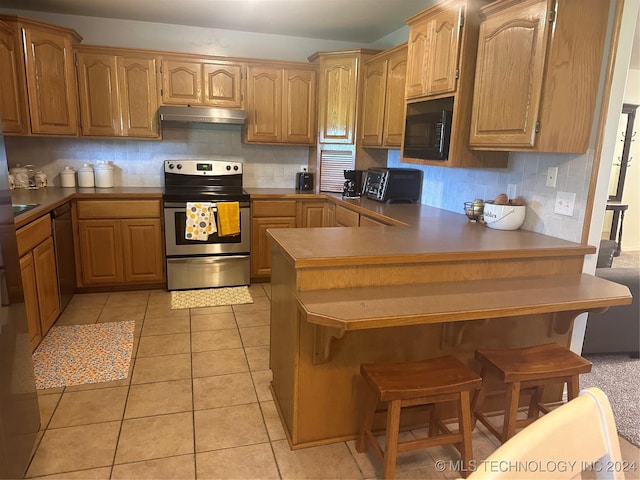 kitchen with a kitchen breakfast bar, kitchen peninsula, decorative backsplash, light tile patterned floors, and appliances with stainless steel finishes