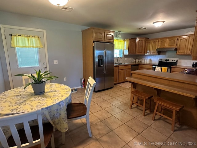 kitchen with sink, a kitchen breakfast bar, backsplash, light tile patterned floors, and appliances with stainless steel finishes