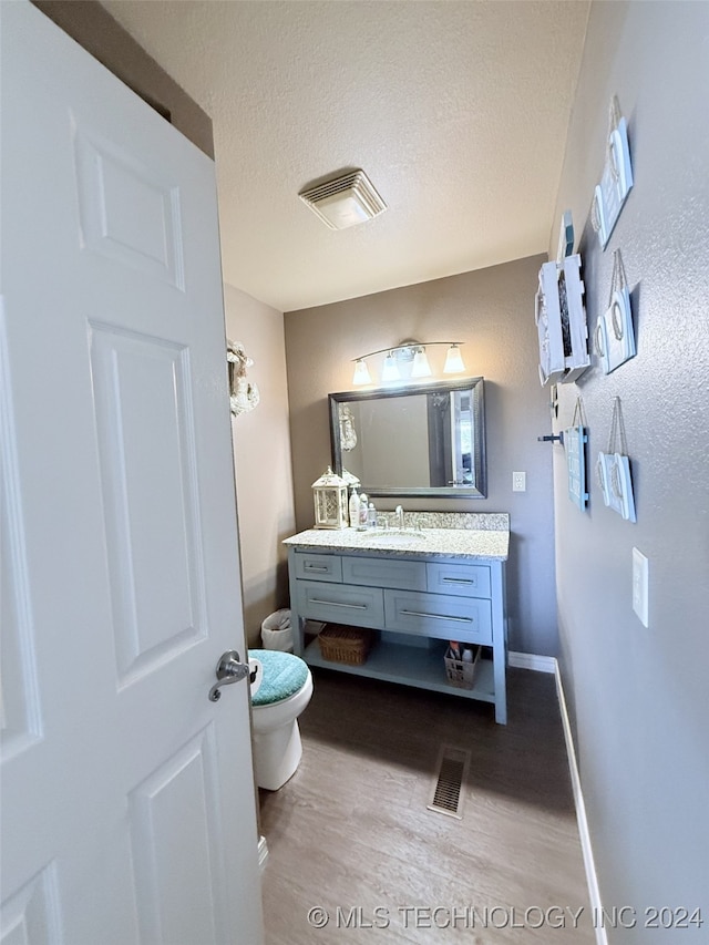 bathroom featuring a textured ceiling, vanity, hardwood / wood-style flooring, and toilet