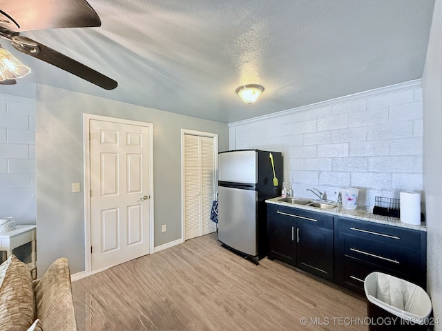 kitchen featuring light stone countertops, light wood-type flooring, a textured ceiling, sink, and stainless steel refrigerator