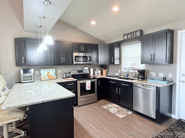 kitchen with kitchen peninsula, stainless steel appliances, vaulted ceiling, decorative light fixtures, and a breakfast bar area