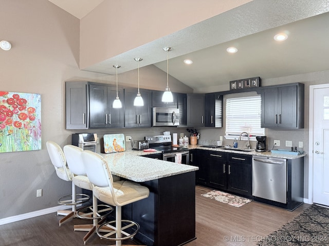 kitchen featuring kitchen peninsula, appliances with stainless steel finishes, a kitchen breakfast bar, decorative light fixtures, and lofted ceiling