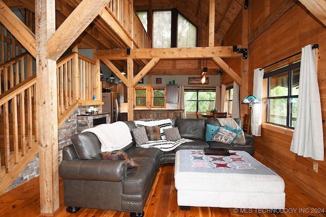 living room featuring beam ceiling, hardwood / wood-style flooring, high vaulted ceiling, and wood walls