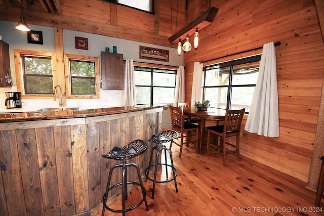 kitchen featuring light wood-type flooring, wooden walls, sink, beam ceiling, and decorative light fixtures