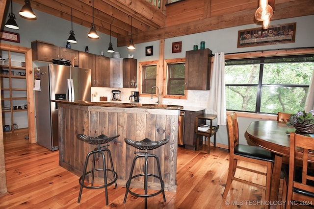 kitchen with stainless steel refrigerator with ice dispenser, beam ceiling, decorative light fixtures, light hardwood / wood-style flooring, and a kitchen island