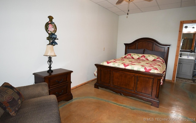 bedroom featuring concrete flooring, a paneled ceiling, ensuite bathroom, and ceiling fan