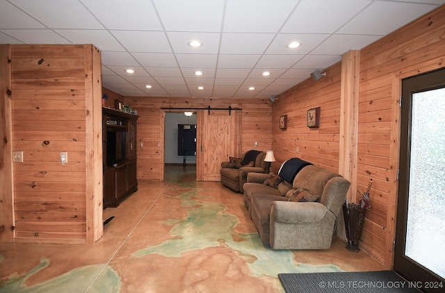 living room with a paneled ceiling, a barn door, and wooden walls