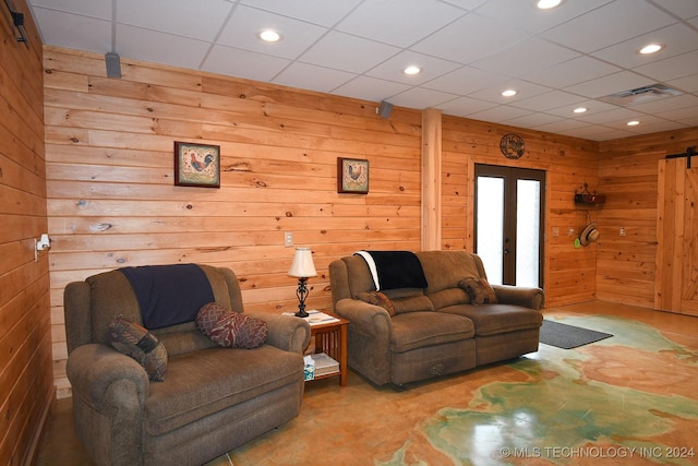 living room with a paneled ceiling, wood walls, a barn door, and french doors