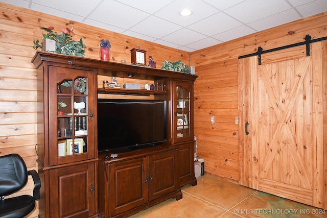 tiled living room with a barn door, wood walls, and a drop ceiling