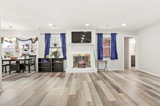 unfurnished living room with a brick fireplace, light hardwood / wood-style flooring, and a notable chandelier