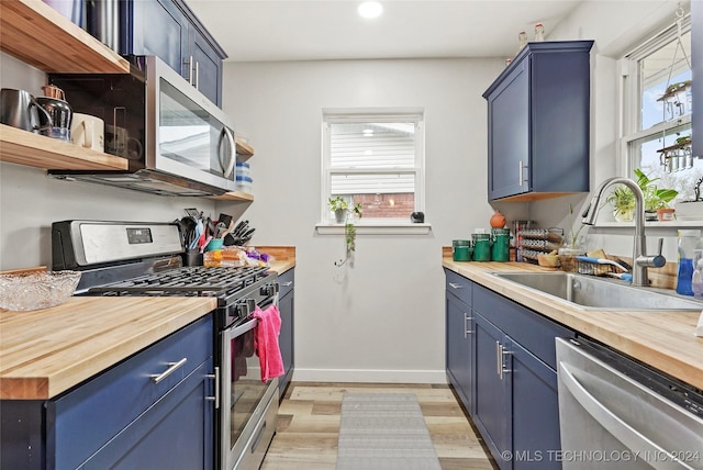 kitchen with blue cabinetry, butcher block countertops, stainless steel appliances, and a wealth of natural light