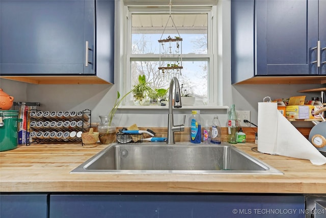 kitchen featuring decorative light fixtures, wood counters, blue cabinets, and sink