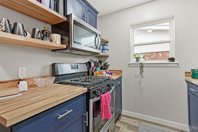 kitchen featuring butcher block countertops, light hardwood / wood-style floors, blue cabinetry, and appliances with stainless steel finishes