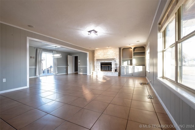 unfurnished living room featuring a fireplace, built in shelves, tile patterned floors, and plenty of natural light