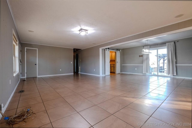 empty room with a barn door, light tile patterned floors, and ornamental molding