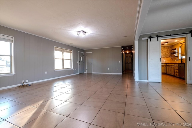 spare room with a barn door, a wealth of natural light, crown molding, and light tile patterned floors