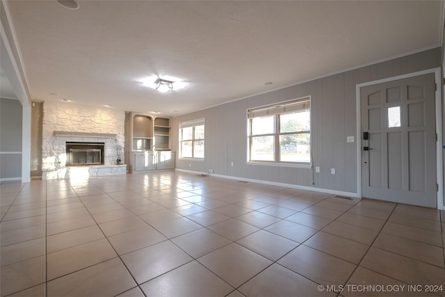 unfurnished living room featuring ornamental molding, a textured ceiling, built in features, a stone fireplace, and light tile patterned flooring