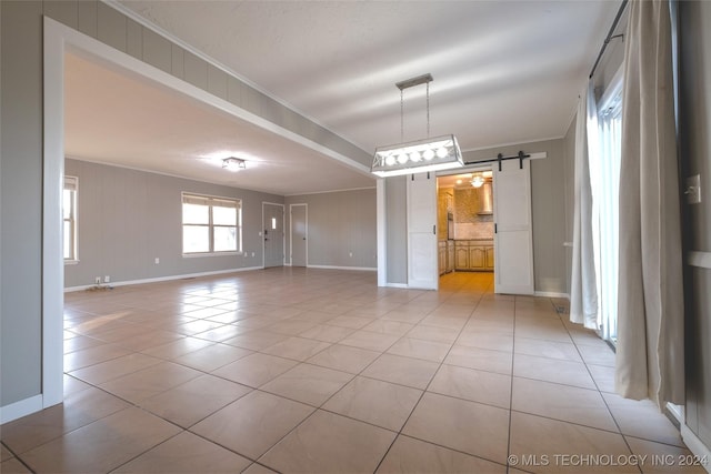 empty room with light tile patterned floors, a barn door, and crown molding