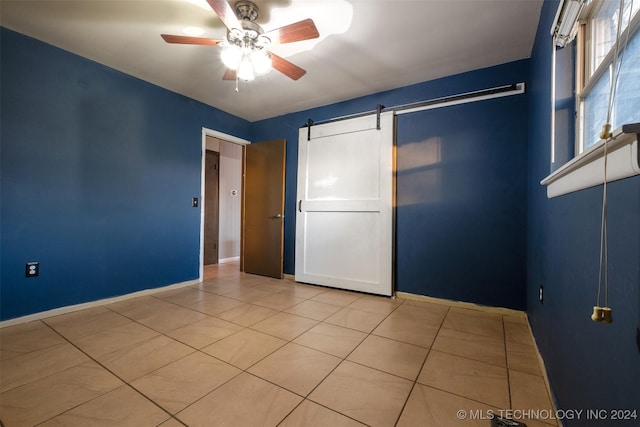 unfurnished bedroom with a barn door, ceiling fan, and light tile patterned floors