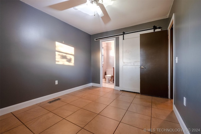 unfurnished bedroom featuring light tile patterned floors, a barn door, ceiling fan, and connected bathroom