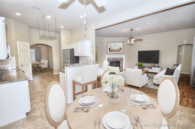 dining area with ceiling fan, light tile patterned flooring, sink, and a brick fireplace