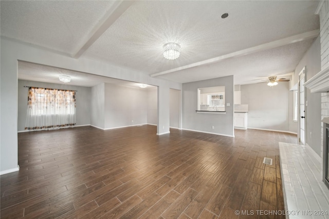 unfurnished living room featuring a textured ceiling, beam ceiling, dark wood-type flooring, and a brick fireplace