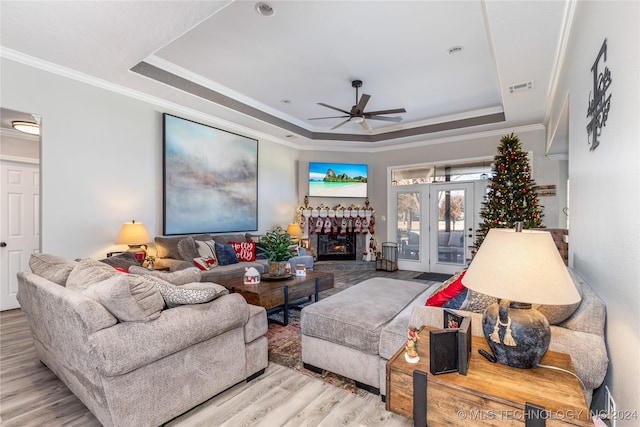 living room with a raised ceiling, ornamental molding, and light wood-type flooring