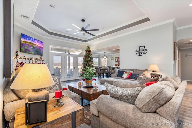 living room with ceiling fan, a raised ceiling, wood-type flooring, and crown molding