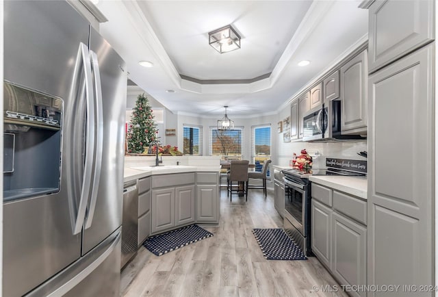 kitchen featuring gray cabinetry, stainless steel appliances, a tray ceiling, pendant lighting, and light hardwood / wood-style floors