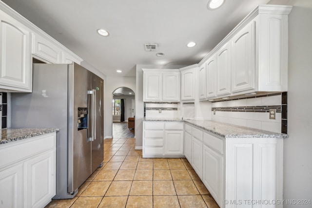 kitchen featuring stainless steel fridge, tasteful backsplash, light stone counters, light tile patterned floors, and white cabinets