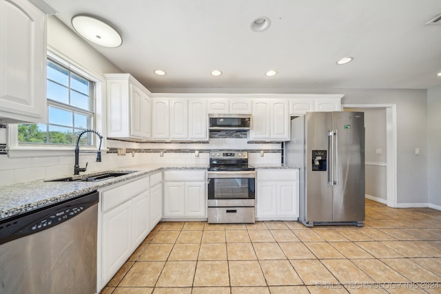 kitchen featuring white cabinets, backsplash, light stone counters, and stainless steel appliances