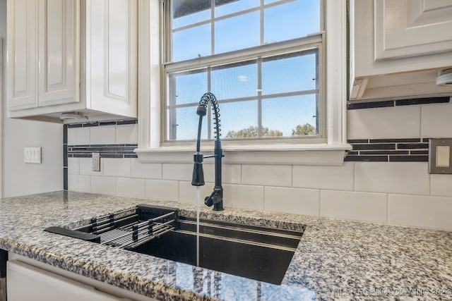 interior details featuring decorative backsplash, white cabinetry, sink, and light stone counters