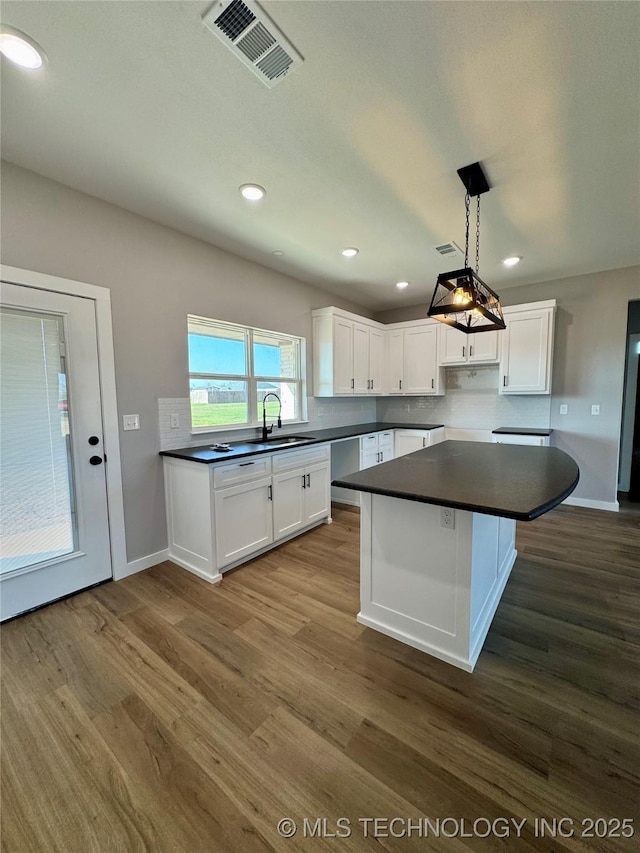 kitchen featuring visible vents, dark wood-style flooring, a sink, white cabinets, and dark countertops