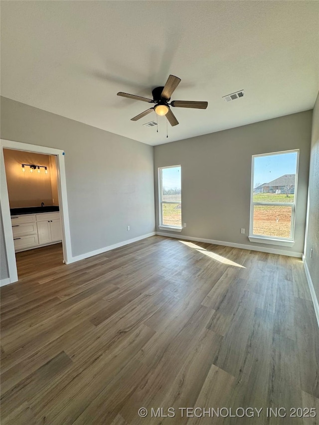 unfurnished bedroom with visible vents, multiple windows, baseboards, and wood finished floors