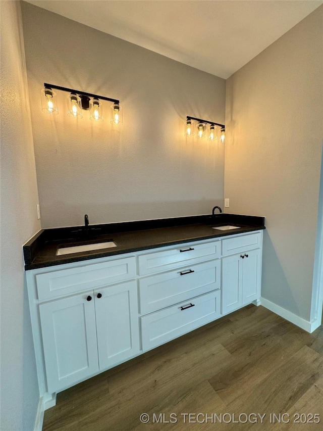 bathroom with double vanity, wood finished floors, baseboards, and a sink