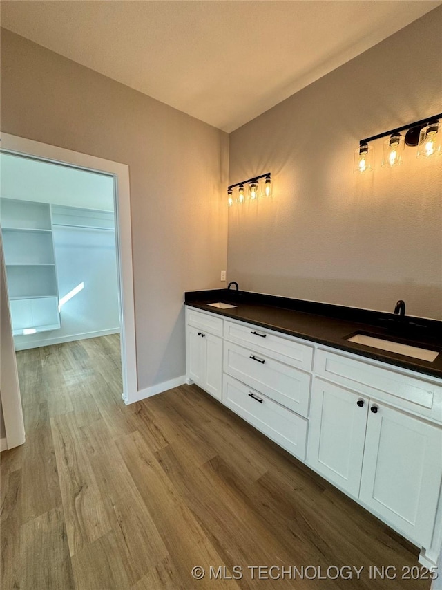 full bath featuring double vanity, wood finished floors, baseboards, and a sink