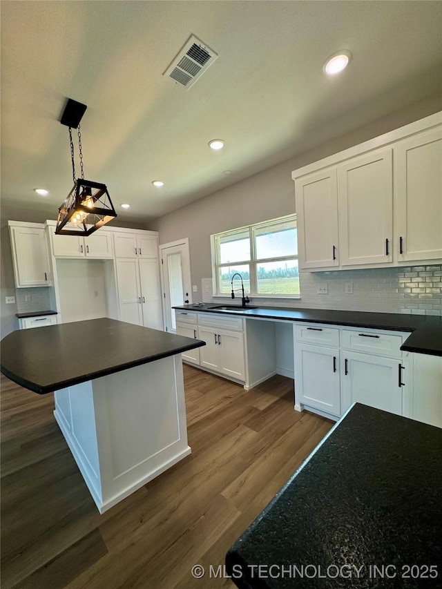 kitchen featuring dark countertops, visible vents, dark wood-type flooring, decorative backsplash, and white cabinets