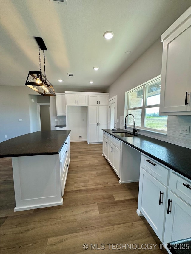kitchen with a sink, wood finished floors, dark countertops, and white cabinets