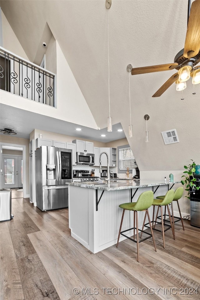 kitchen featuring high vaulted ceiling, white cabinets, hanging light fixtures, kitchen peninsula, and stainless steel appliances