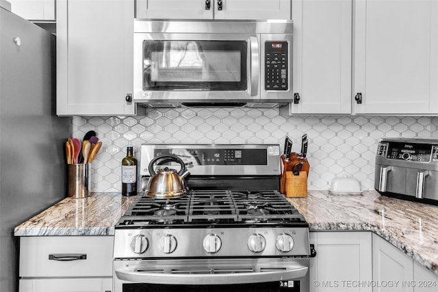 kitchen featuring decorative backsplash, appliances with stainless steel finishes, white cabinetry, and light stone counters