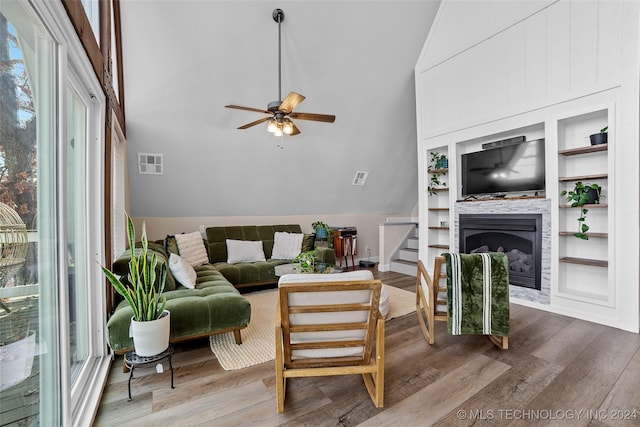 living room with wood-type flooring, high vaulted ceiling, ceiling fan, and built in shelves