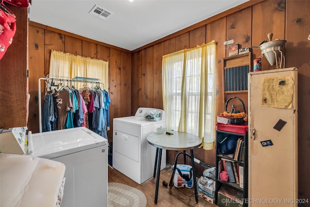 clothes washing area with wood walls, washer and dryer, and light wood-type flooring