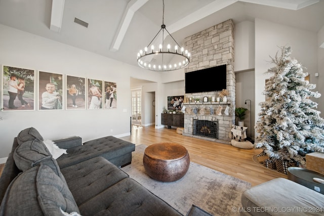 living room with wood-type flooring, high vaulted ceiling, a stone fireplace, and a notable chandelier