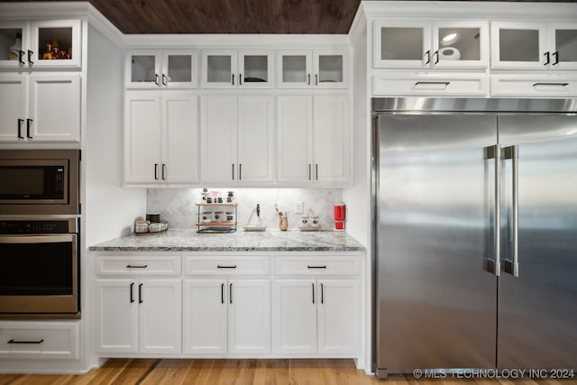 kitchen featuring built in appliances, light stone countertops, and white cabinetry