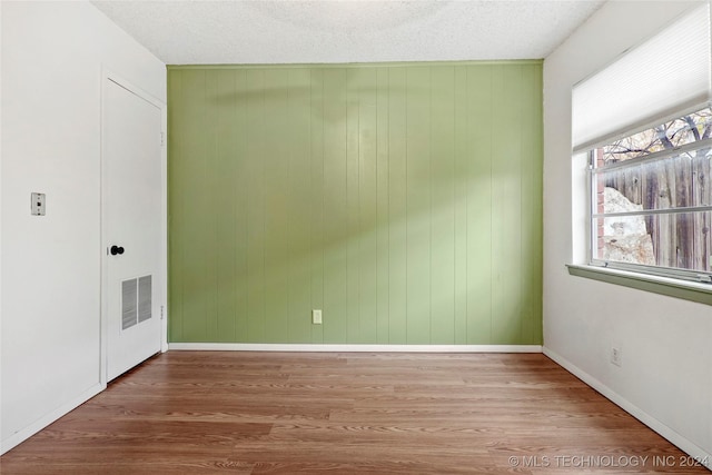 spare room with hardwood / wood-style flooring, wood walls, and a textured ceiling